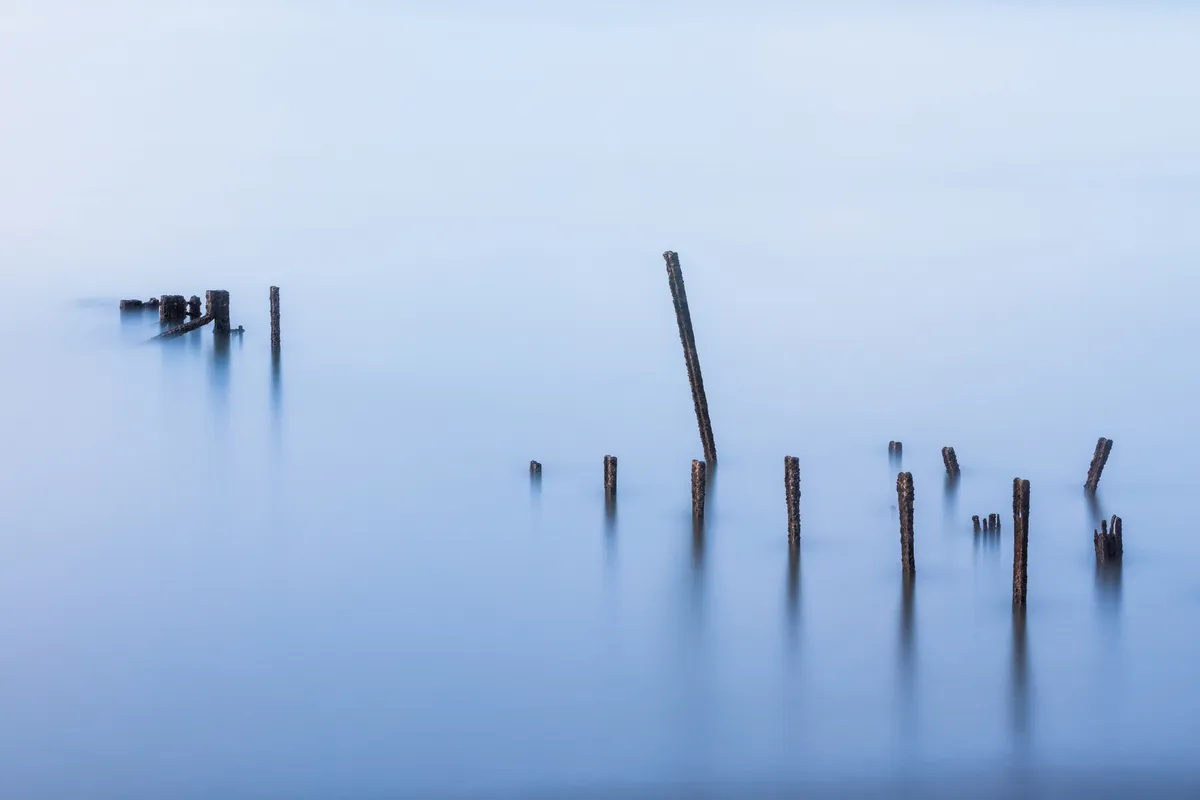 Weathered jetty posts emerging from calm long-exposure water at Newhaven in East Sussex