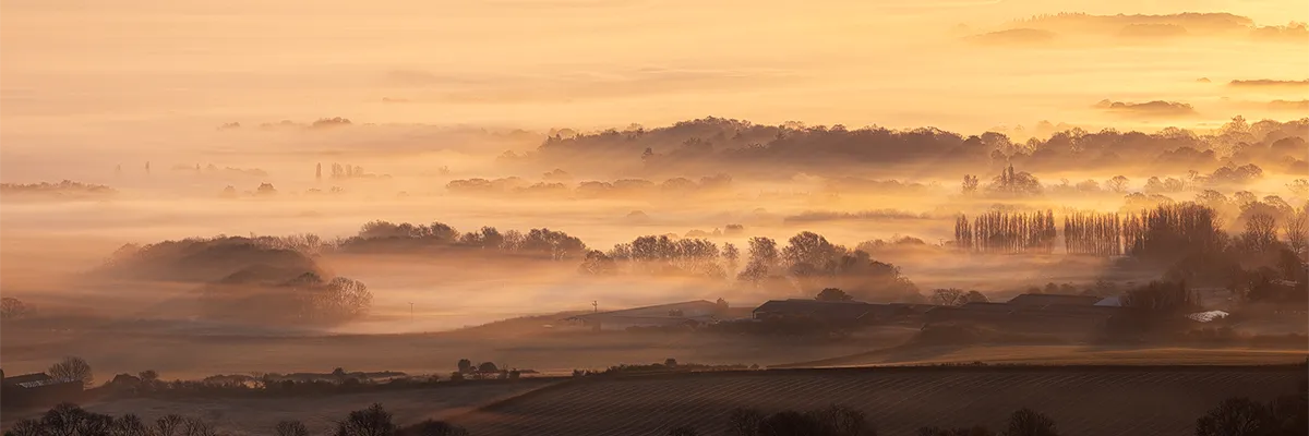 Golden morning mist rolling across layered countryside at Ditchling Beacon in East Sussex
